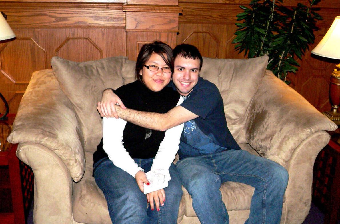 A male student hugs a female student while both sit in a plush chair